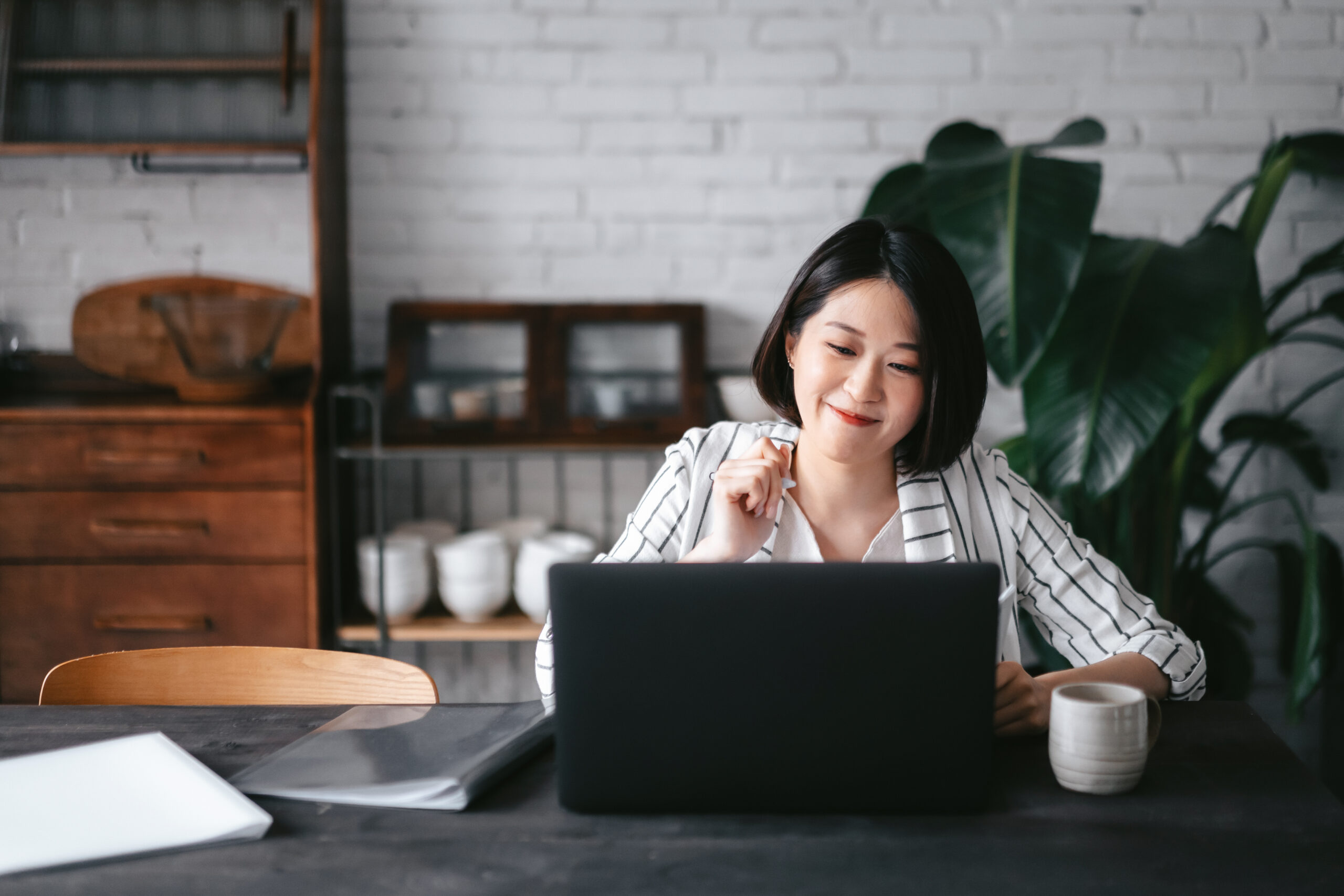 Young Asian woman having online business meeting, video conferencing on laptop with her business partners, working from home in the living room